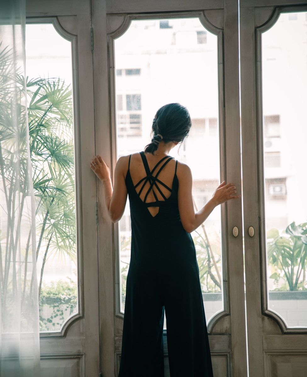 woman in black and red tank top standing near white wooden framed glass window